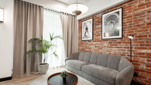 Un salon avec un canapé gris, une table basse ronde, une plante en pot et un mur en briques orné de deux tableaux encadrés.