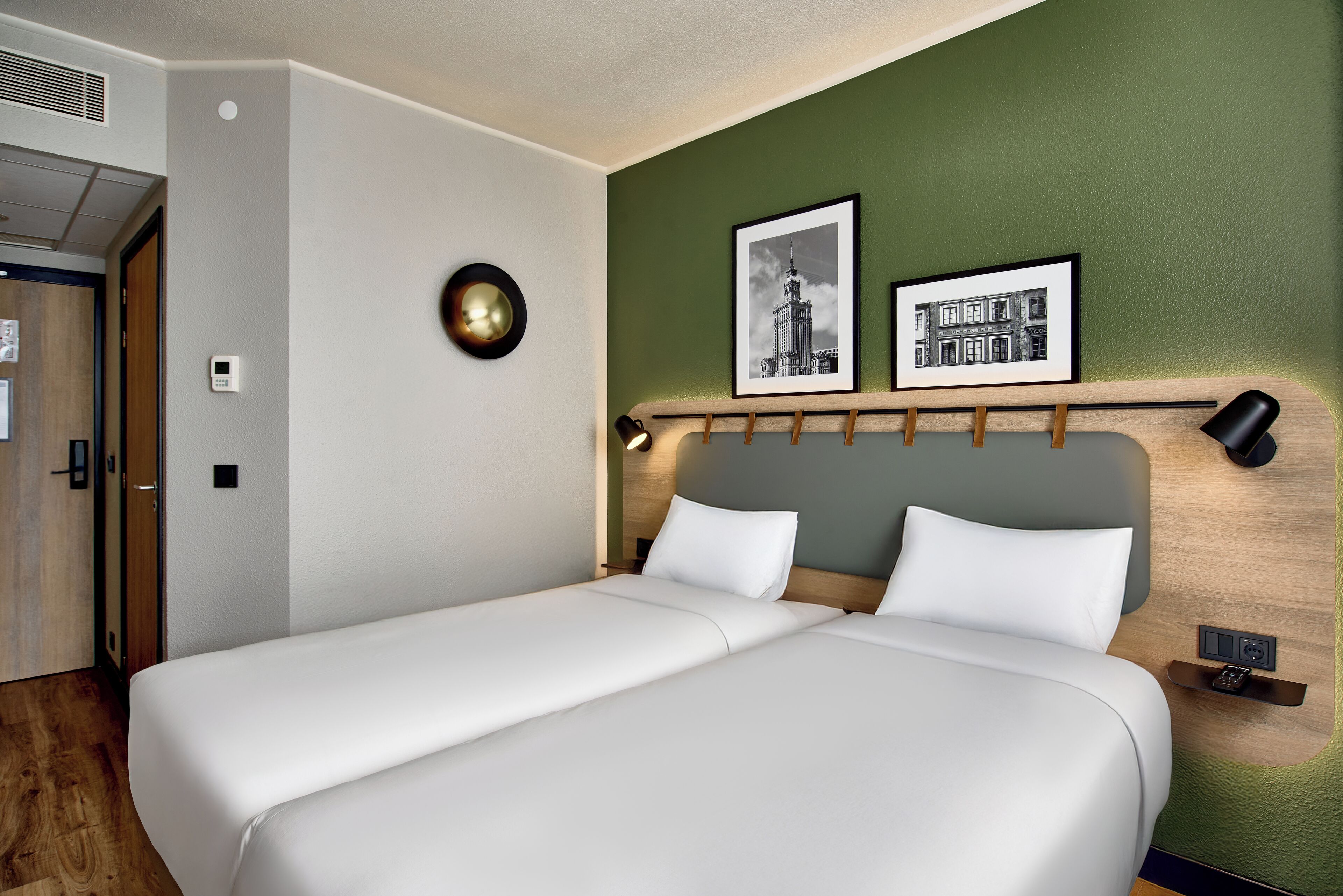 Ein Doppelbett mit weißer Bettwäsche, ein Nachttisch mit Lampe und zwei gerahmte Bilder an der Wand.