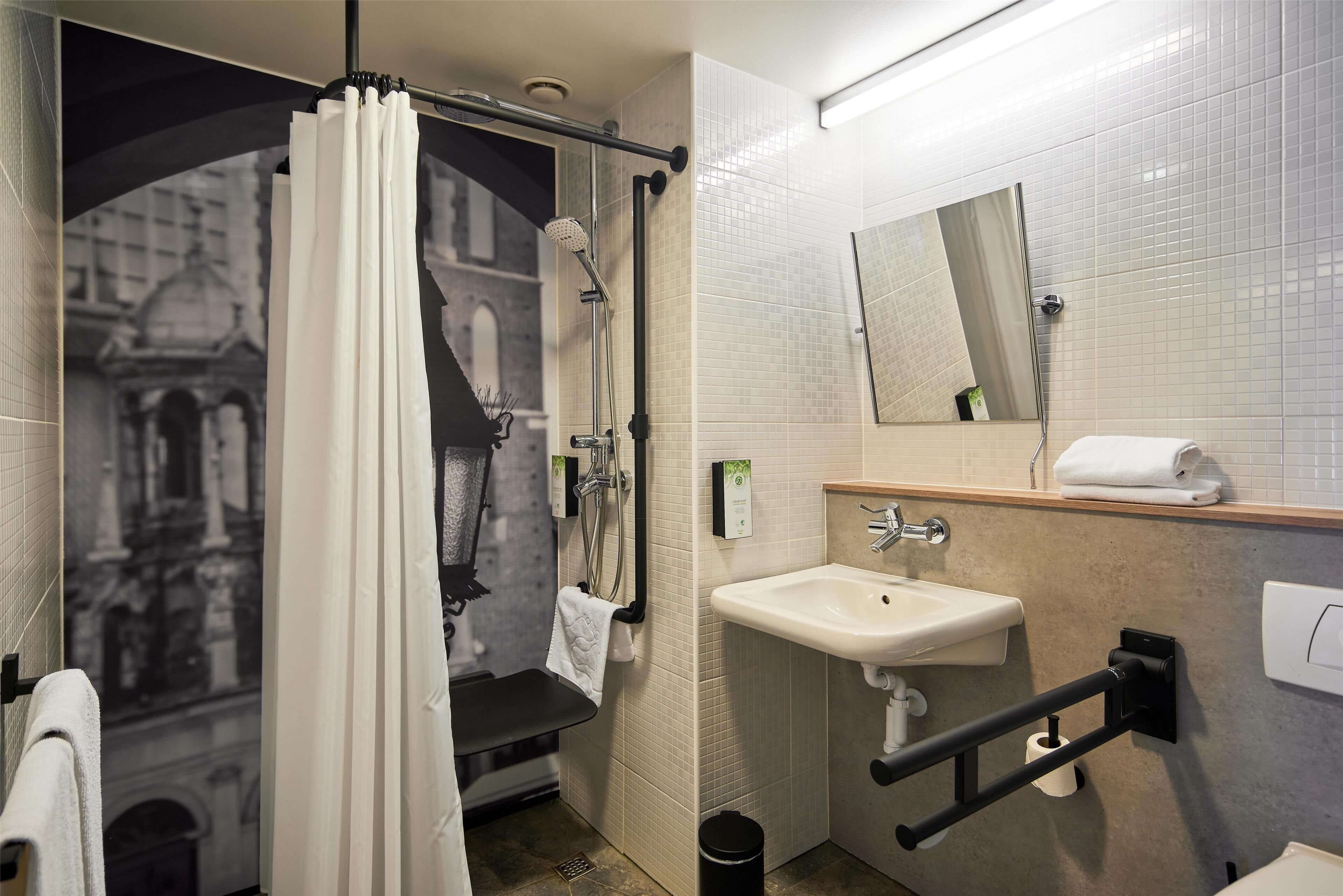 A bathroom with a shower, a sink, a mirror, and a towel rack.