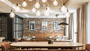 Un espace repas moderne avec des tables rondes, des chaises marron, des murs en briques apparentes et des luminaires suspendus.