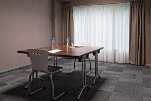 Une salle de conférence avec une table en bois, deux chaises et une grande fenêtre avec des rideaux.