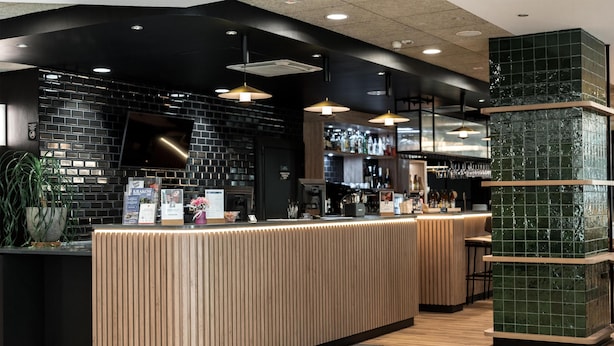 Un espace bar moderne avec un comptoir en bois, un mur en briques noires et des suspensions lumineuses.