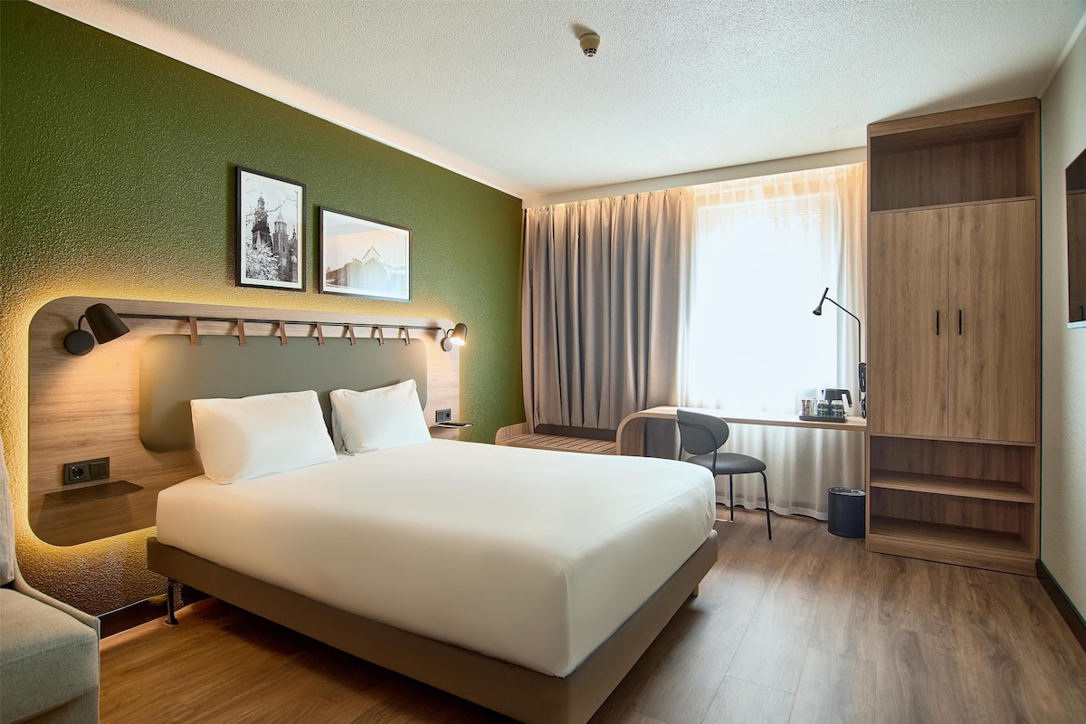 Een hotelkamer met een groot bed, een bureau met stoel, een kledingkast en een raam met gordijnen.