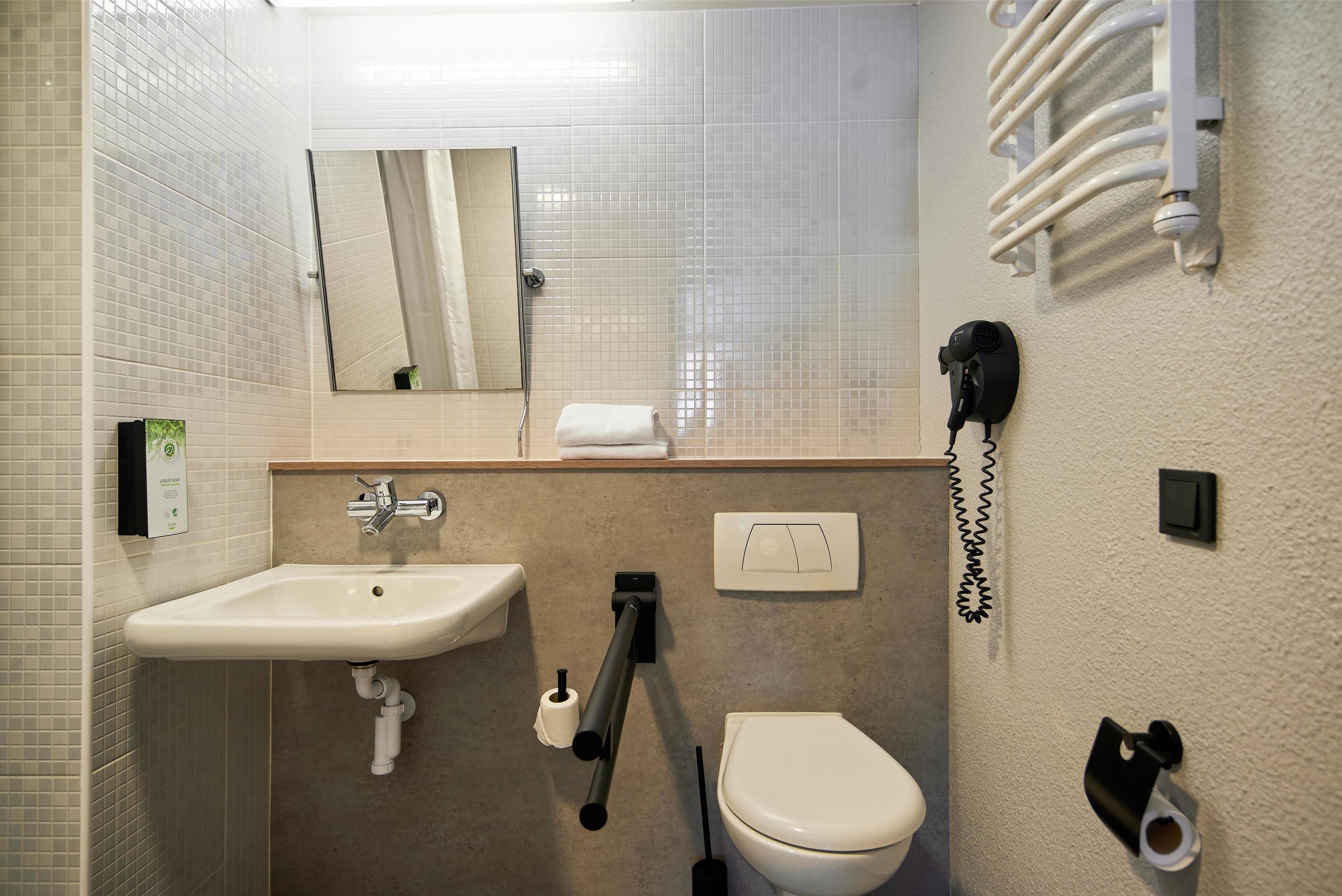 A bathroom with a sink, toilet, towel dispenser, and a mirror.