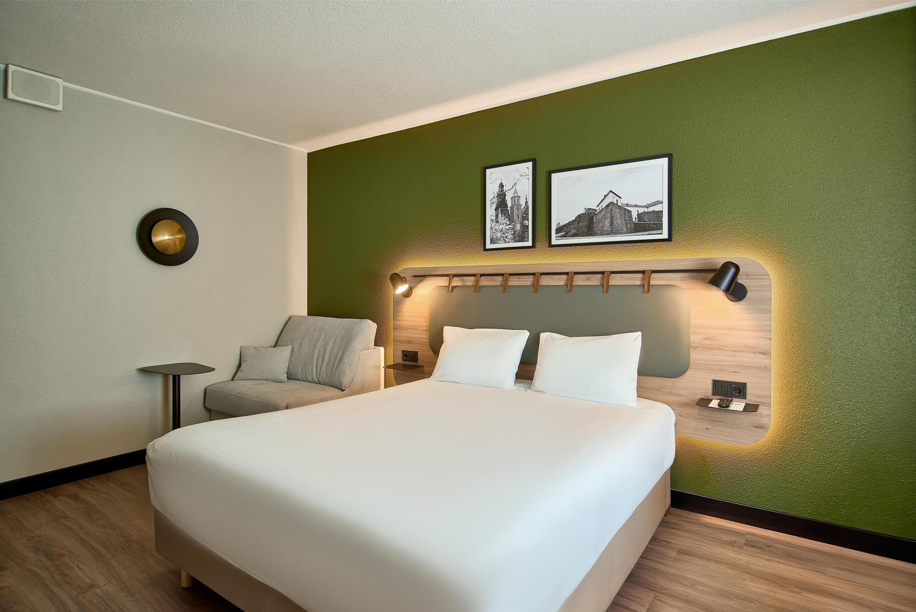 A hotel room with a large bed, a small seating area, and a green accent wall.