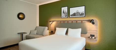 A hotel room with a large bed, a small seating area, and a green accent wall.