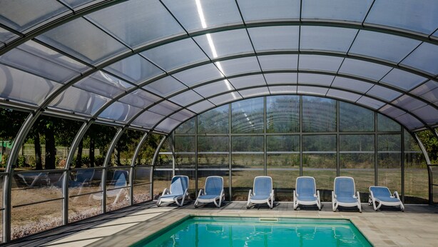Ein überdachter Swimmingpool mit Liegestühlen und einer Glaskonstruktion.