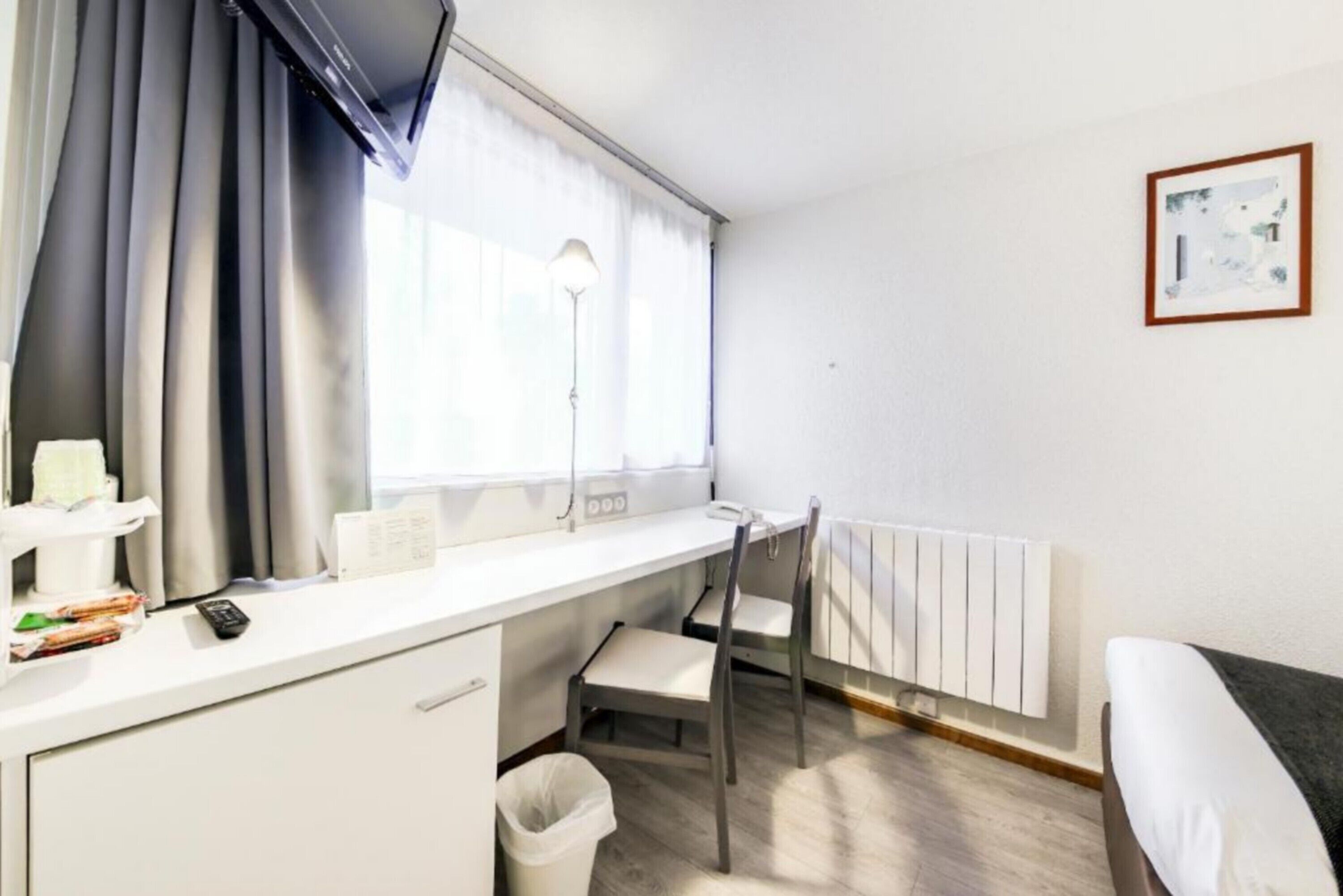 A hotel room with a desk, chair, radiator, and a bed.