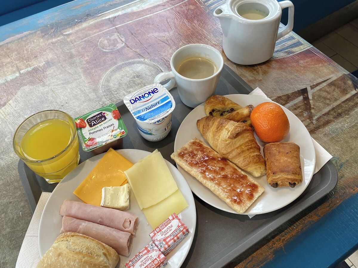 A tray with breakfast items including croissants, ham, cheese, an orange, juice, coffee, and Danone yogurt.