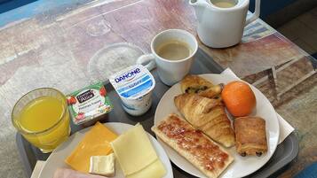 A tray with breakfast items including croissants, ham, cheese, an orange, juice, coffee, and Danone yogurt.