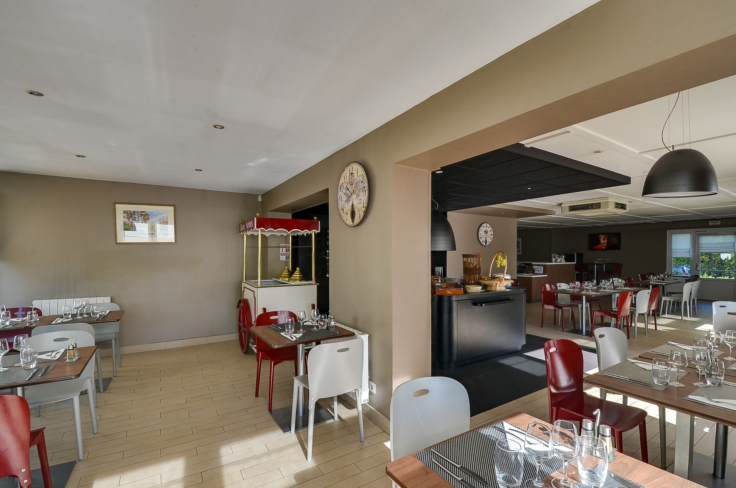 A restaurant with tables set for dining, a kitchen area, and a clock on the wall.