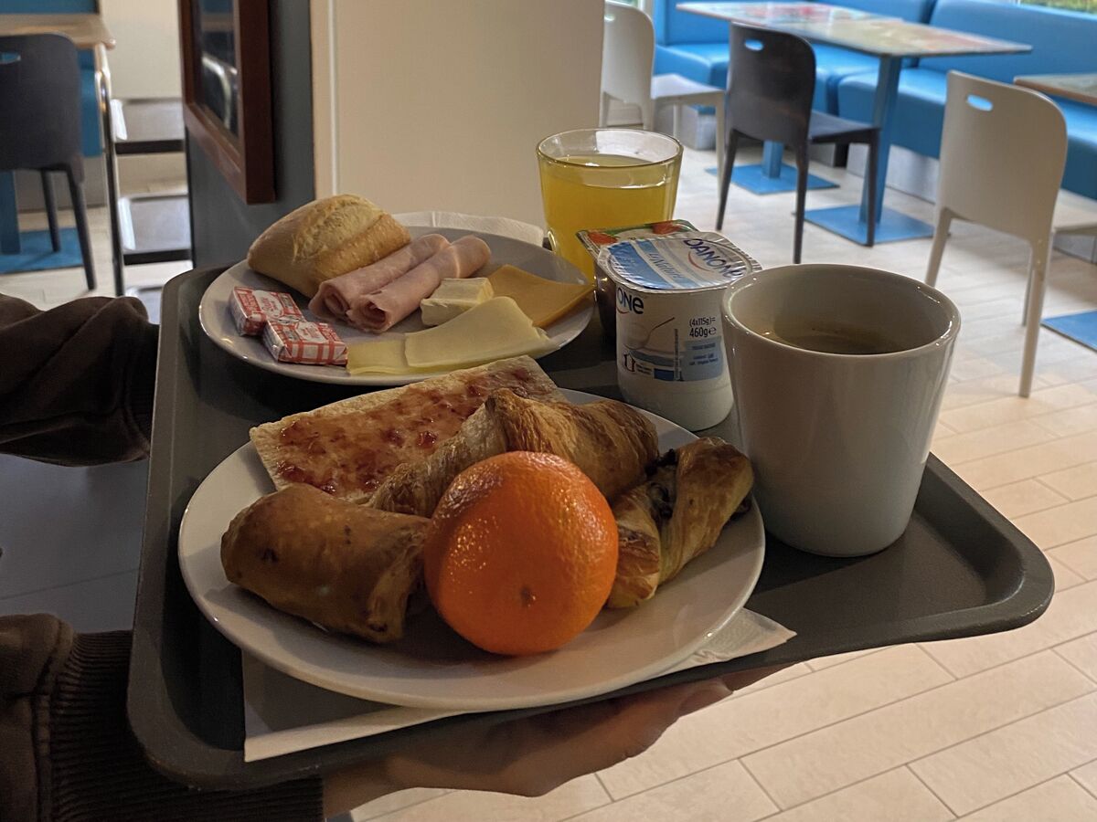 Un vassoio per la colazione con croissant, prosciutto, formaggio, un'arancia e una tazza di caffè.
