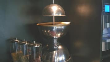 A kitchen area with a coffee machine, a red pot, and stacked plates.