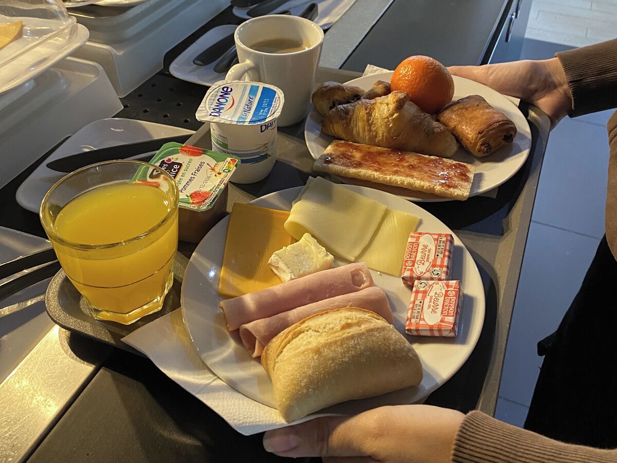 Uma bandeja com itens de café da manhã, incluindo croissants, presunto, queijo, suco e café.