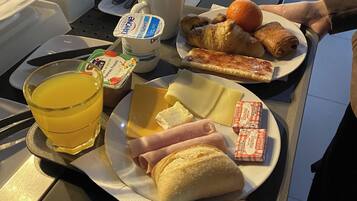 Uma bandeja com itens de café da manhã, incluindo croissants, presunto, queijo, suco e café.