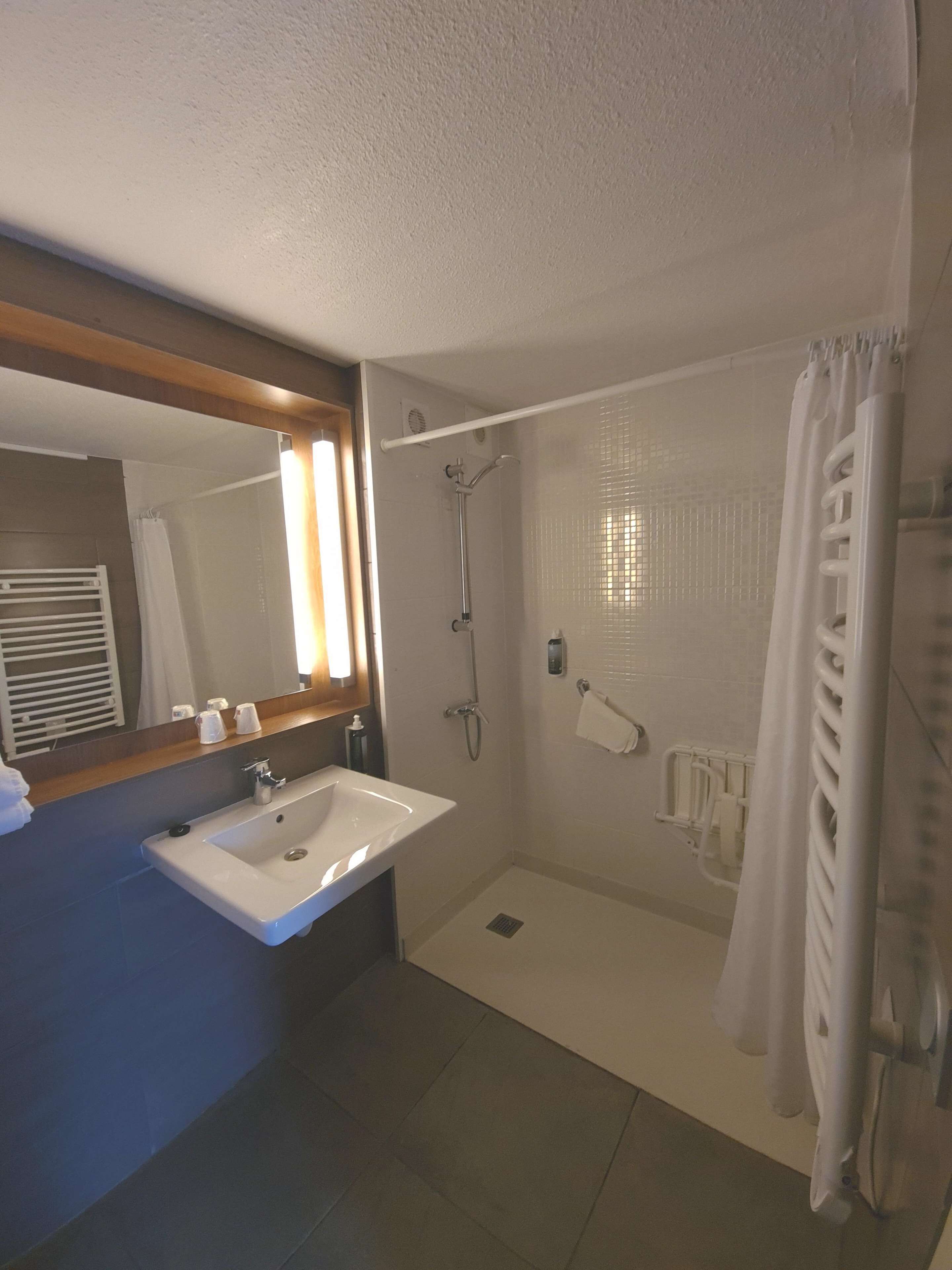 A bathroom with a sink, mirror, shower, and towel rack.