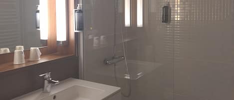 A bathroom with a glass-enclosed shower, a sink with a mirror above it, and a wooden countertop.