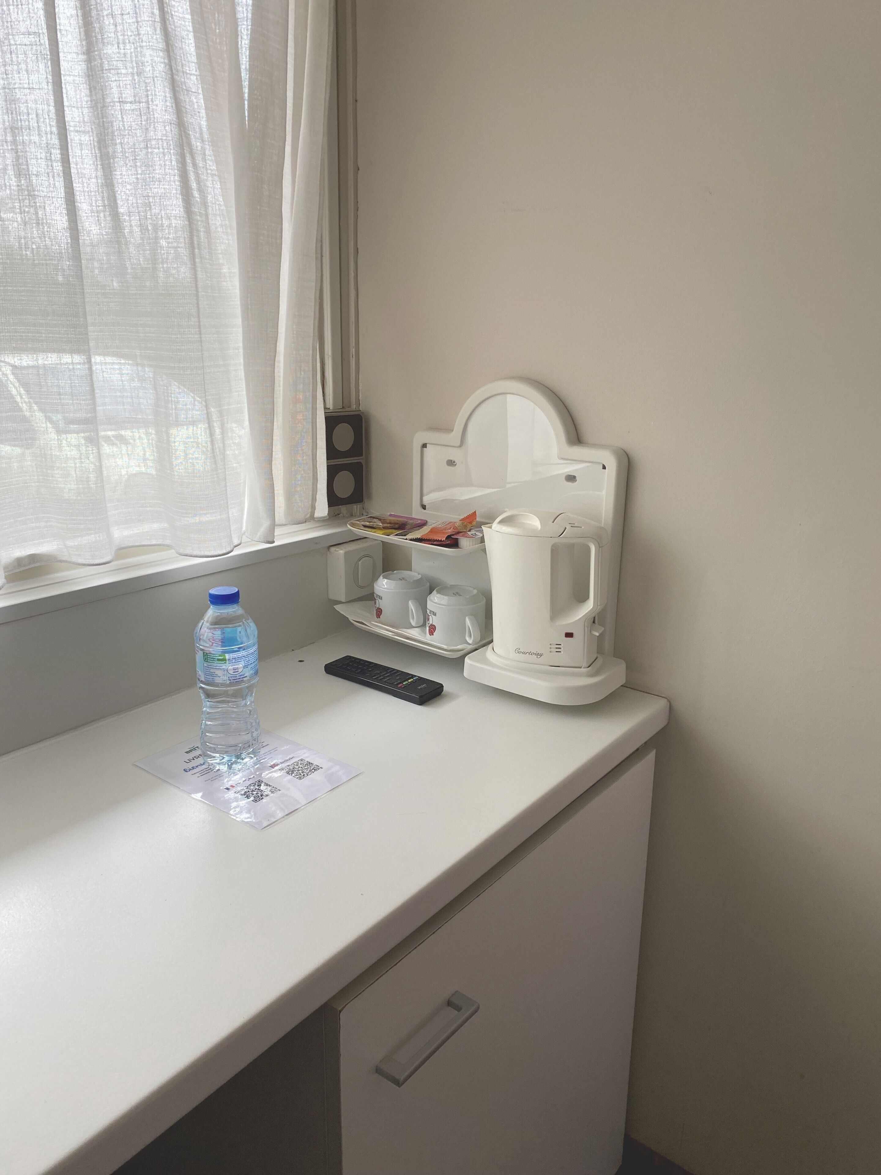 A small kitchenette with a coffee maker, a water bottle, and a remote control on a white countertop.