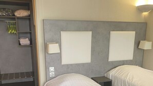 Ein Hotelzimmer mit zwei Betten, einem Kleiderschrank und einem Nachttisch mit Lampen.
