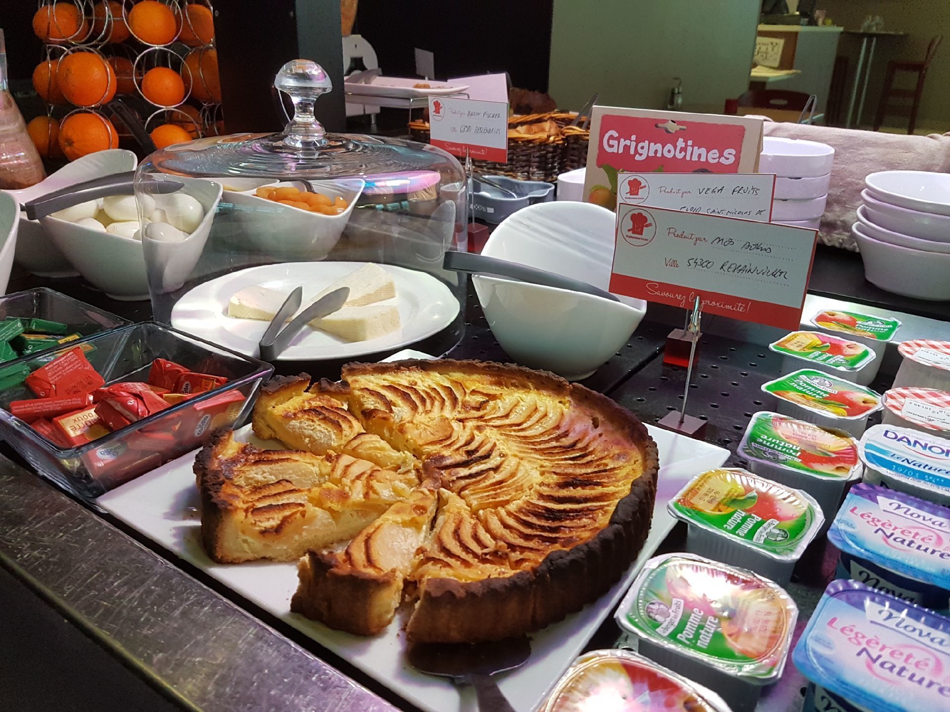 Un bufé con diversos alimentos, incluyendo una tarta de manzana grande, fuentes de fruta y recipientes de yogur.