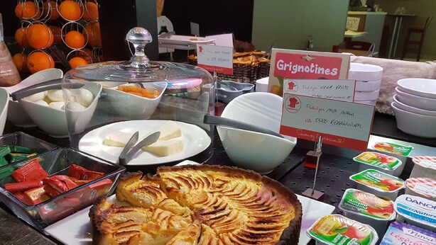 Een buffet met diverse soorten eten, waaronder een grote appeltaart, schalen met fruit en bakjes yoghurt.