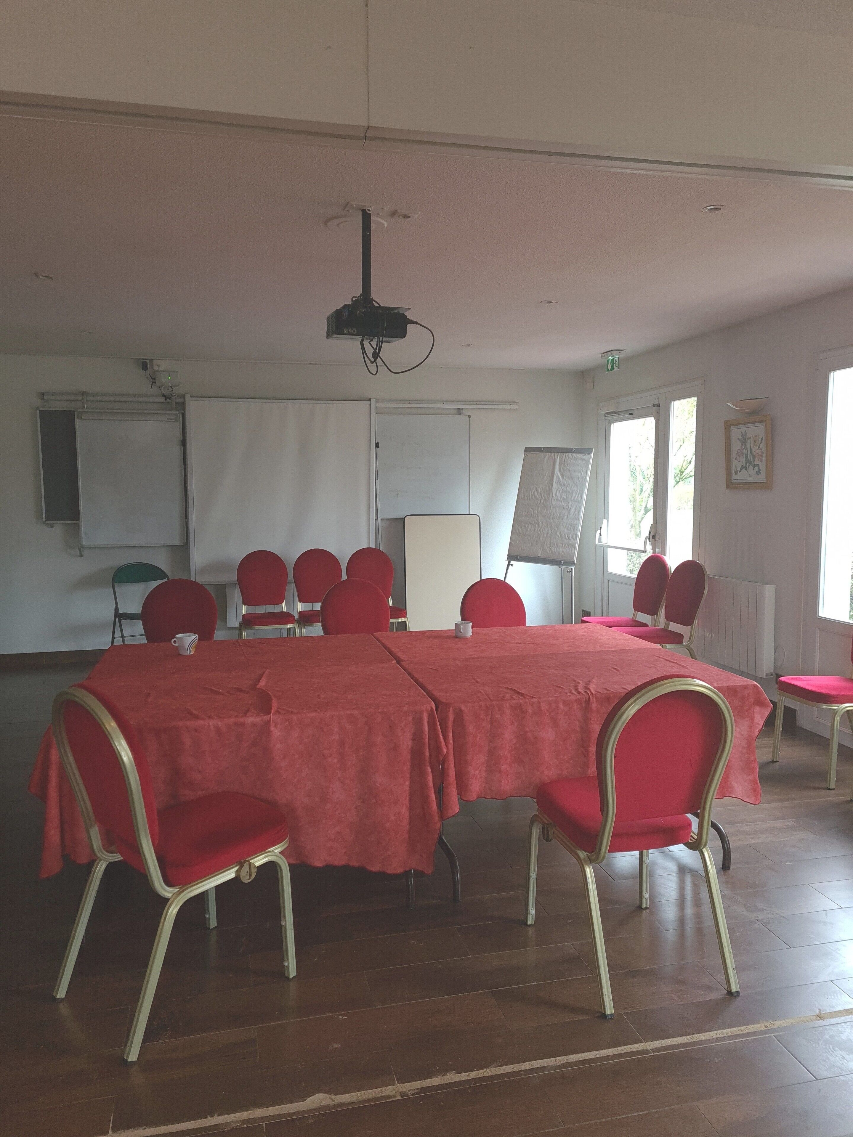 Ein Konferenzraum mit einem großen, roten Tisch, umgeben von roten Stühlen, einem Projektor und einer Whiteboard-Tafel.