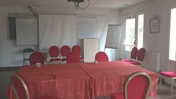 Ein Konferenzraum mit einem großen, roten Tisch, umgeben von roten Stühlen, einem Projektor und einer Whiteboard-Tafel.