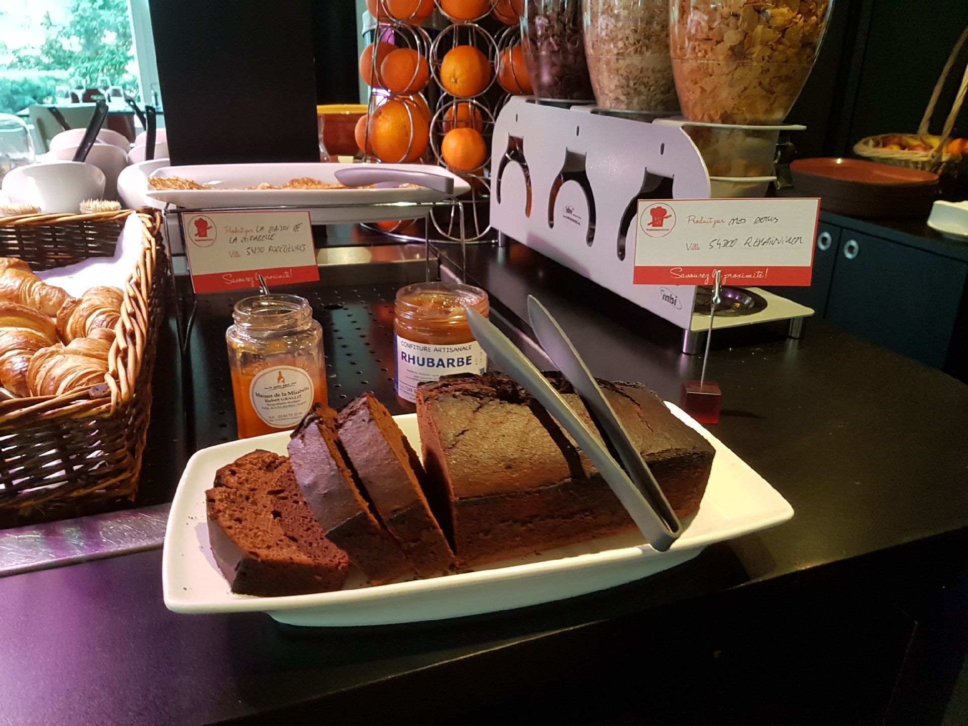 A buffet with a variety of food items including bread, pastries, and a chocolate cake.