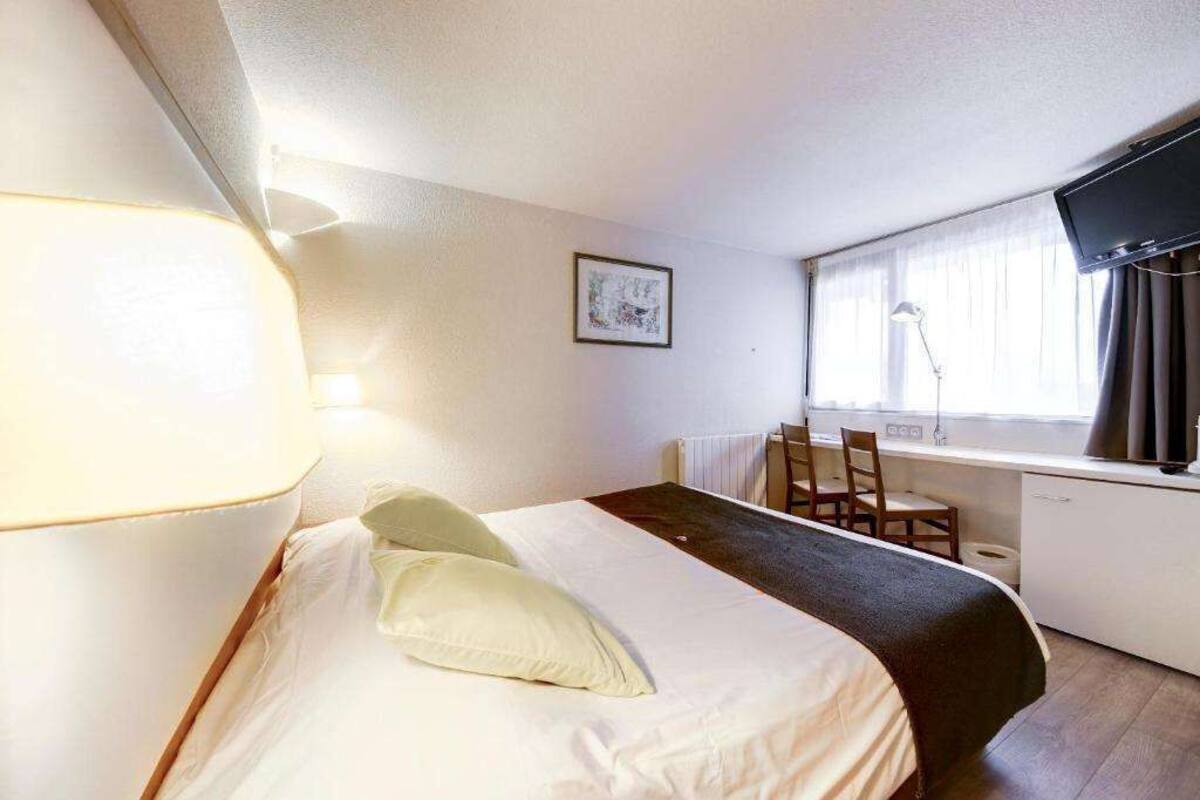 A hotel room with a bed, a desk, a chair, a TV, and a window with curtains.