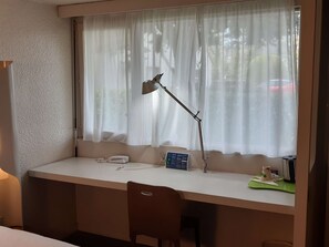 Un petit bureau privé, équipé d’un bureau, d’une chaise et d’une fenêtre ornée de rideaux légers.