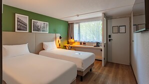 A hotel room with two beds, a desk with a lamp, a window with curtains, and framed pictures on the wall. - Hotel Campanile Grenoble Nord - Saint Egrève (Saint-Egreve)
