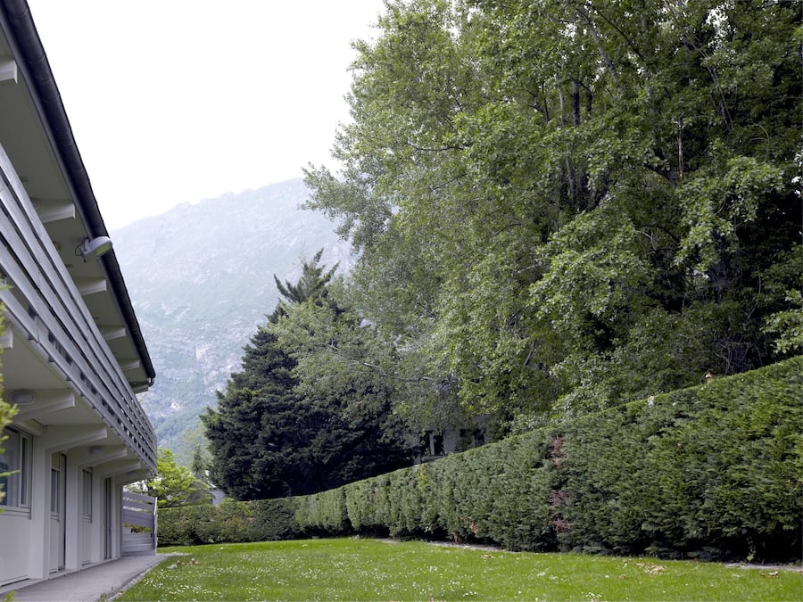 A building with a covered outdoor area, surrounded by well-maintained greenery and mountains in the background.