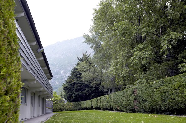A building with a covered outdoor area, surrounded by well-maintained greenery and mountains in the background.