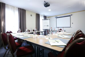 A conference room with a long table, red chairs, name placards, water bottles, and a projector screen.