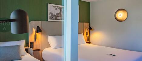A hotel room with two beds, wall-mounted lamps, a framed picture, and a round light fixture.