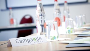 Una mesa de conferencias con una placa que dice "Campanile Business" y varias botellas de agua.