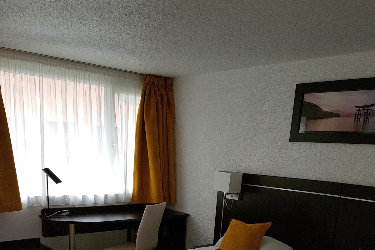 A hotel room with two beds, a desk, a chair, and a window with curtains.