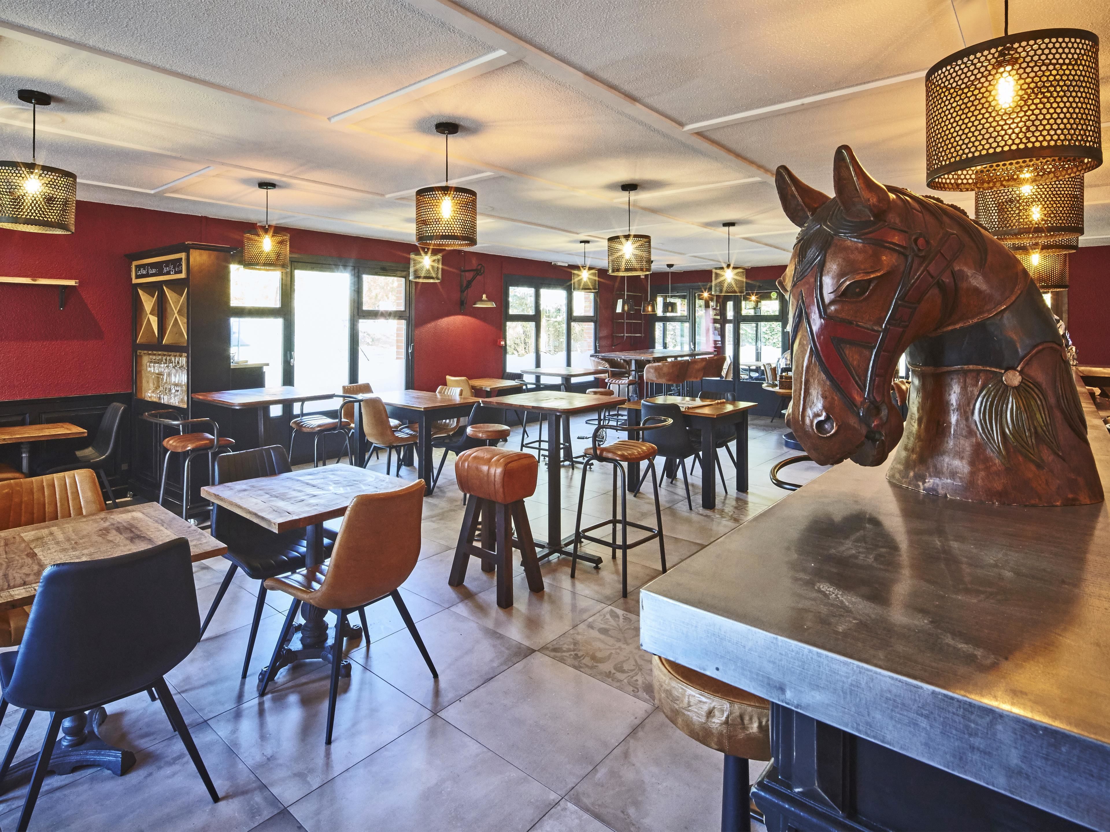 Interior de restaurante con mesas altas, sillas, lámparas colgantes y una gran escultura de caballo.
