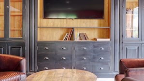 A modern living room with leather sofas, a wooden coffee table, a large flat-screen TV mounted on a wooden wall, and a dark-colored cabinet with drawers. - Kyriad Lille Est - Hem (Hem)