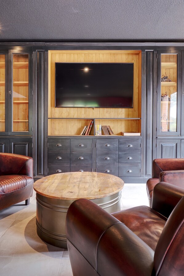 A modern living room with leather sofas, a wooden coffee table, a large flat-screen TV mounted on a wooden wall, and a dark-colored cabinet with drawers.