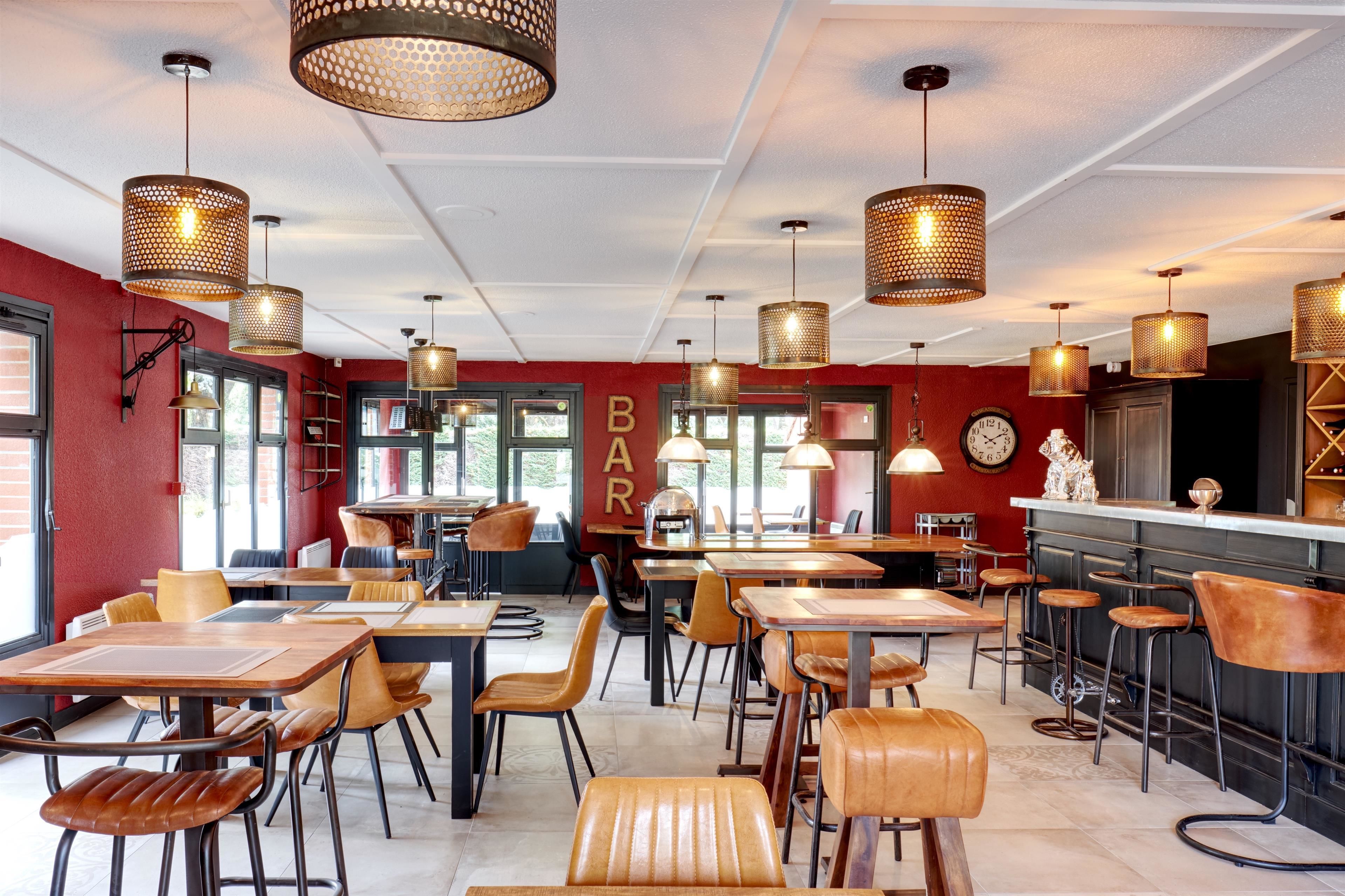 Un restaurant avec des tables et des chaises hautes, des luminaires suspendus et un espace bar.