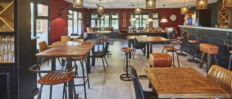 Un interior de restaurante con varias mesas y sillas de madera, lámparas colgantes y una zona de bar.