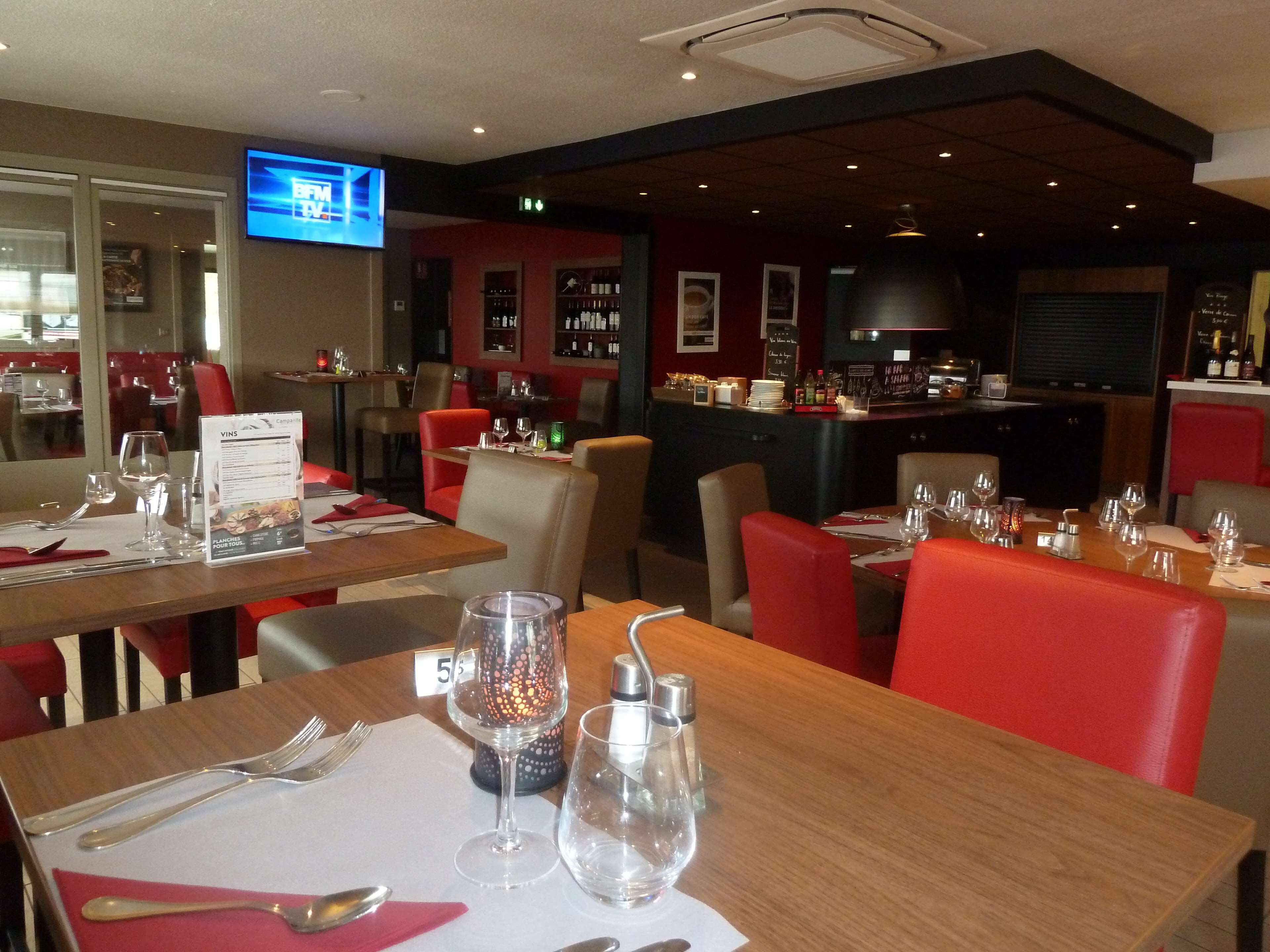 A restaurant with tables set for dining, a bar area, and a television screen displaying a news channel.