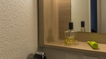 Une salle de bain avec un miroir, un sèche-cheveux et un flacon de lotion posé sur le comptoir.