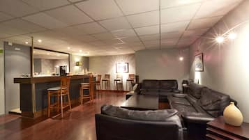 A modern living room with a black leather sofa, a dining area with wooden chairs, and a kitchen counter.