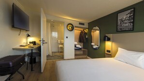 A hotel room with a bed, a desk with a chair, a TV, a closet with a mirror, and a bathroom visible through an open door. - Campanile NATURE - Le Mans Est (Le Mans)