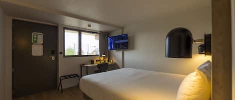 Habitación de hotel con cama, escritorio, silla, televisor y ventana.