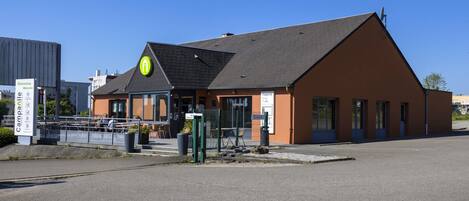 A building with a sloped roof and a green sign with a yellow arrow.