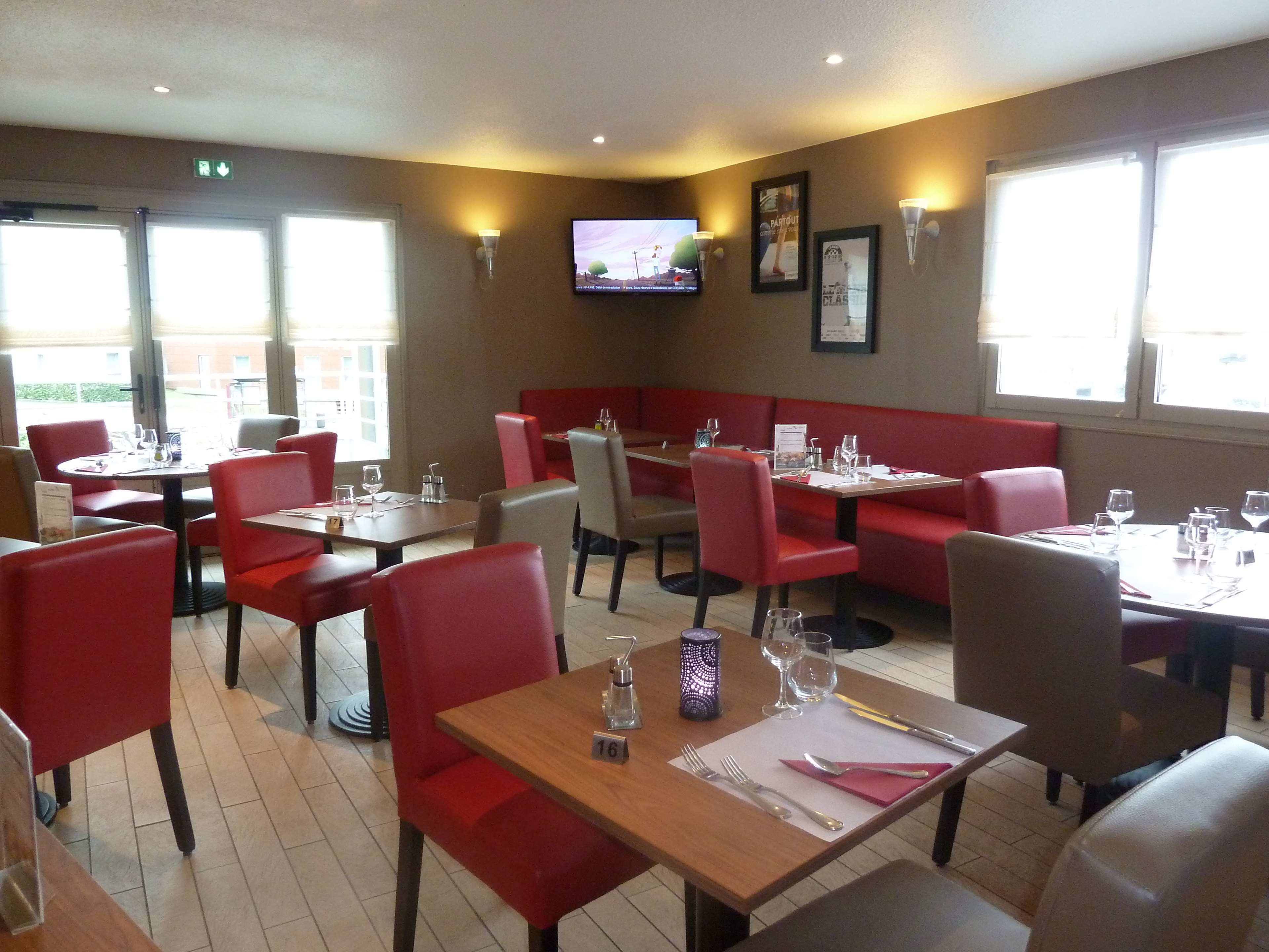 A restaurant with red booths and tables, a TV mounted on the wall, and a menu stand.