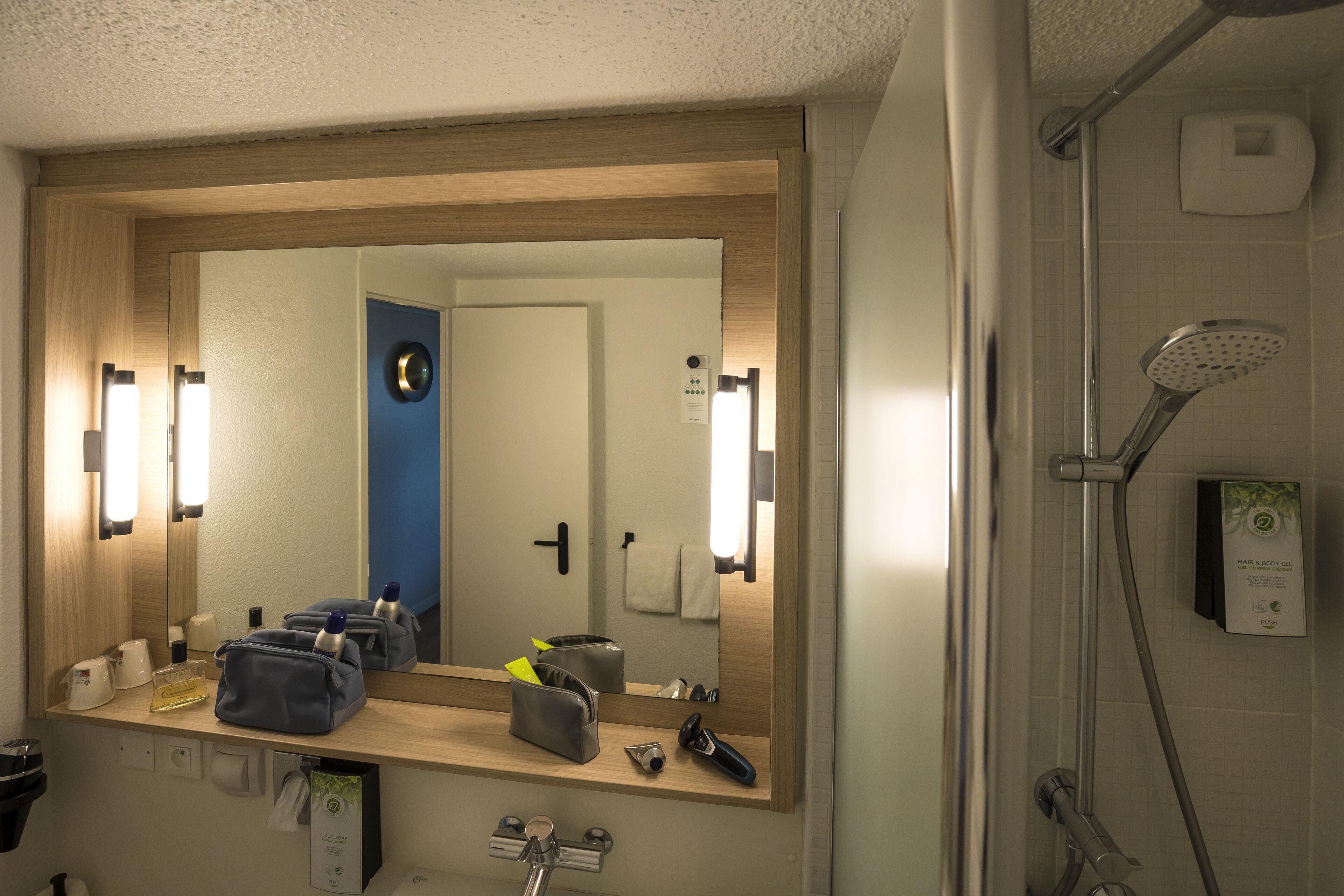 A bathroom with a large mirror, a shower, and a sink.